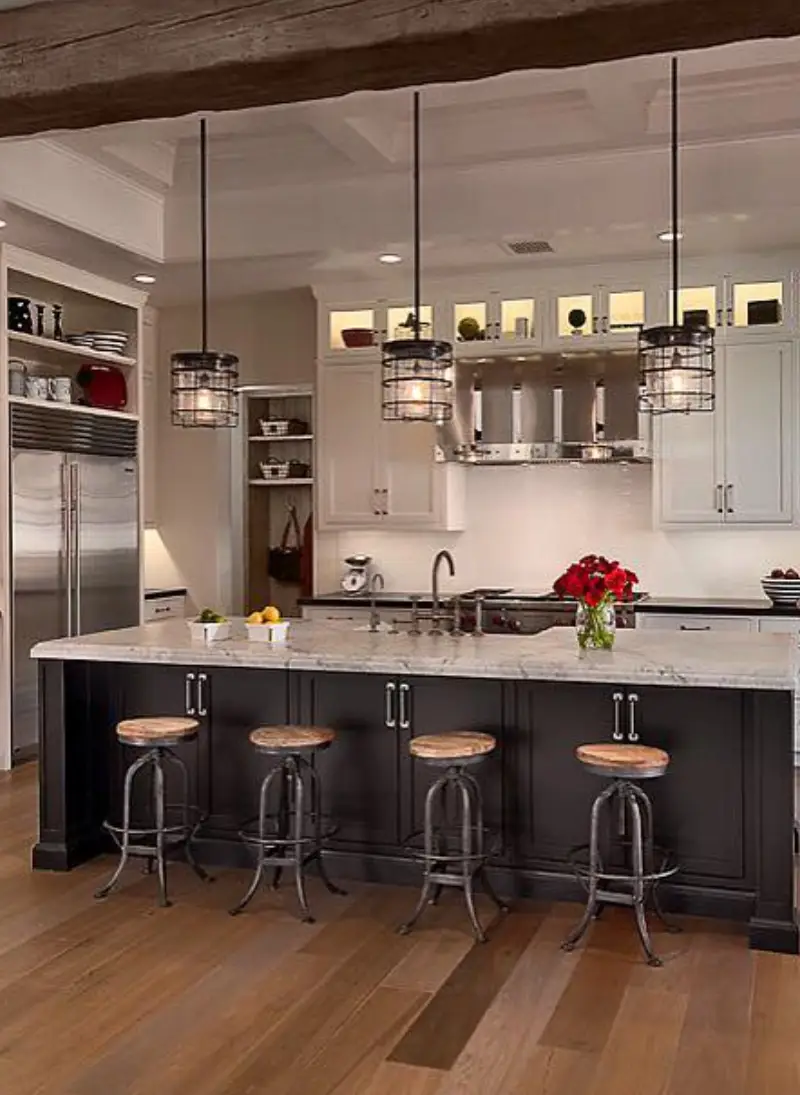 serv3 webp Modern kitchen featuring white cabinetry, a marble island with four stools, pendant lights, and stainless steel appliances in warm tones.